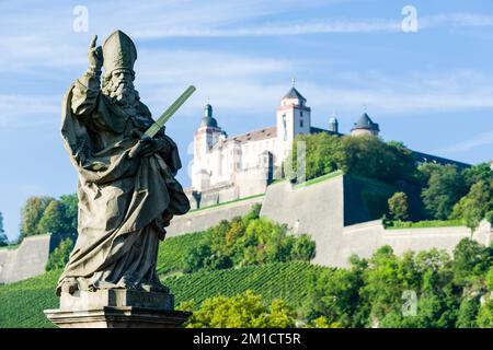 Eine Skulptur des Heiligen Kilian auf der Brücke 'Alte Mainbrücke' und das Schloss 'Festung Marienberg' auf einem Hügel in der Ferne Stockfoto