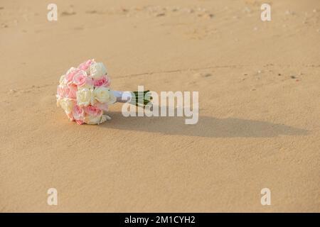 Am Sandstrand befindet sich ein großer Strauß Rosen. Sieht frisch und wunderschön aus, goldenes Sonnenlicht, umgeben von Muscheln Stockfoto