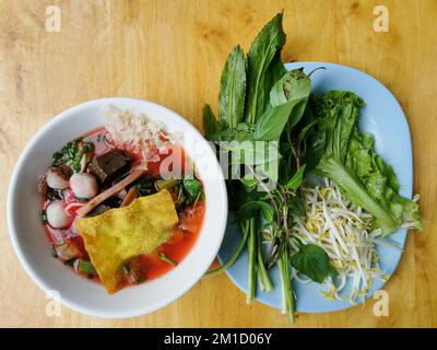 Yen ta fo oder Young tao fo. Eine thailändische Nudelsuppe mit Fischball, Tintenfisch, gebratenem Wanton und Gemüse in einer weißen Schüssel auf Holzhintergrund. Thailändisches Street Food Stockfoto