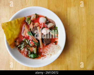 Yen ta fo oder Young tao fo. Eine thailändische Nudelsuppe mit Fischball, Tintenfisch, gebratenem Wanton und Gemüse in einer weißen Schüssel auf Holzhintergrund. Thailändisches Street Food Stockfoto