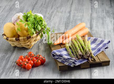 Frischer Spargel, Karotten, Kirschtomaten, Kartoffeln, Knoblauch und Petersilie auf Holzfläche Stockfoto