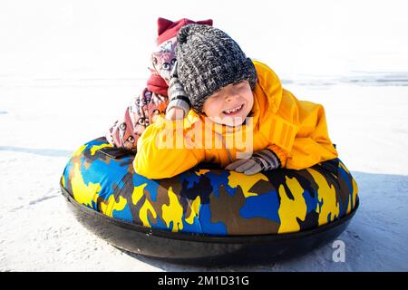 Ein kleiner Junge und ein Mädchen reiten im Winter auf einer Rutsche Stockfoto