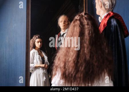 Hübsches Mädchen in weißem Kleid und gruseliger entstellter Mann in schwarzem Stand in Umarmung. Geister-Cosplay, halloween-Feiertagskonzept Stockfoto