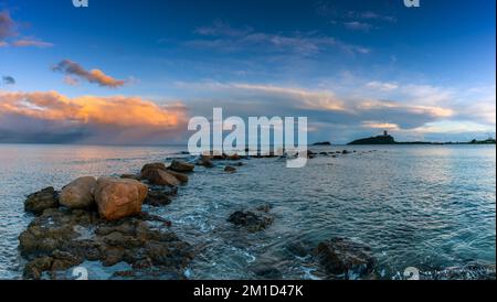 Panoramablick auf einen farbenfrohen Sonnenuntergang am Nora Beach auf Sardinien mit dem Coltellazzo Tower im Hintergrund Stockfoto