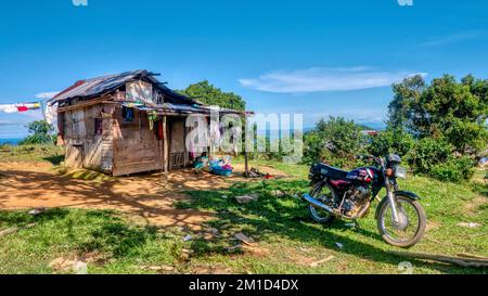 Oriental Mindoro Province, Philippinen - 12. März 2022. Ein Familienhaus, das mit Altmaterial gebaut wurde, und ein Motorrad, das davor geparkt wurde. Stockfoto