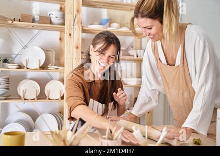 Freunde mit Schürzen in einer Töpferwerkstatt bereiten Ton vor, um Stücke zu kreieren. Handwerksklasse. Stockfoto