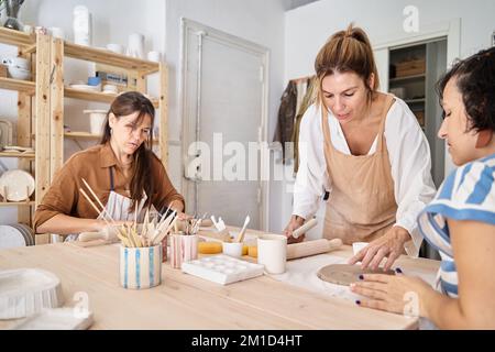 Freunde mit Schürzen in einer Töpferwerkstatt bereiten Ton vor, um Stücke zu kreieren. Handwerksklasse. Stockfoto