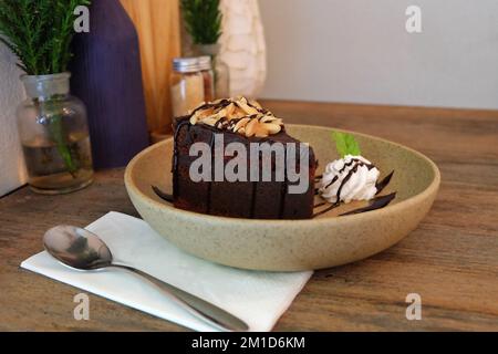 Nahaufnahme: Schokoladen-Fudge-Brownie, garniert mit Mandelscheiben in einer Keramikschüssel Stockfoto