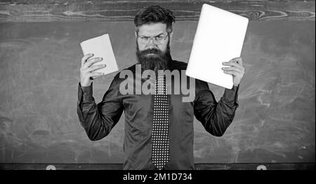 Digital gegen Papier. Der Hipster mit Bart als Lehrer hat ein Buch und einen Laptop. Was wäre dir lieber? Lehrer wählt modernen Lehransatz. Wählen Sie die richtige Stockfoto