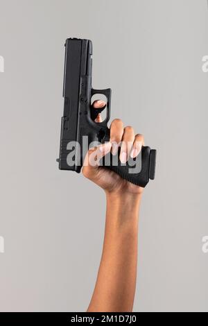 Anonyme afroamerikanische Frau mit schwarzer Handfeuerwaffe auf grauem Hintergrund im Studio Stockfoto