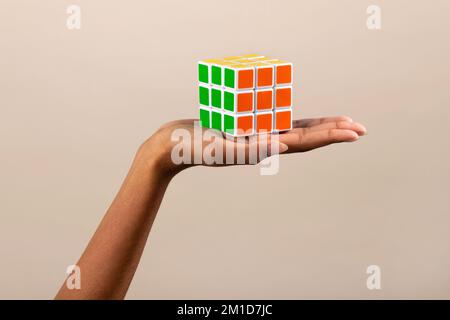 Unerkennbare afroamerikanische Frau, die aufgelösten, bunten Rubiks-Würfel auf beigem Hintergrund vorführt Stockfoto