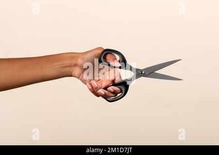 Eine anonyme afroamerikanische Frau mit Metallscheren auf beigefarbenem Hintergrund im Studio Stockfoto