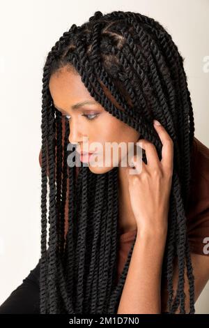 Seitenansicht einer jungen afroamerikanischen Frau mit langen Afro-Geflechten, die das Haar berühren, auf weißem Hintergrund und wegblickend Stockfoto