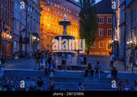 Abend in der Stadt Ljubljana in Slowenien, Menschen am Brunnen auf dem Neuen Platz (Novi Trg). Stockfoto