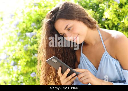 Glückliche Frau, die Handy benutzt und in einem Park sitzt Stockfoto