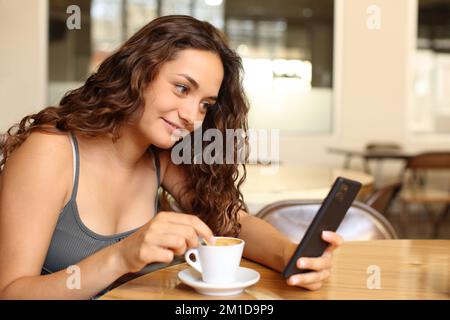 Eine Frau, die in einer Bar auf ihr Smartphone schaut und Kaffee umrührt Stockfoto