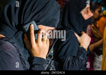 Eine muslimische Frau, die mit Rückenkleidung und Schleier bedeckt ist, benutzt ihr Handy Stockfoto
