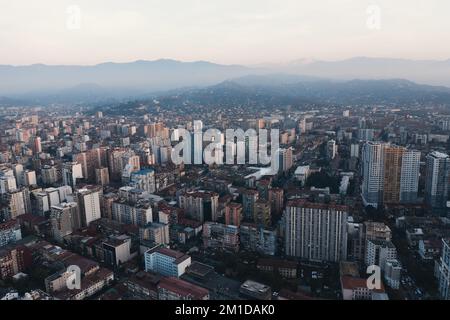 Luftaufnahme von der Drohne auf die nächtlichen Stadtgebäude von Batumi mit Bergen im Hintergrund in der Dämmerung. Stockfoto