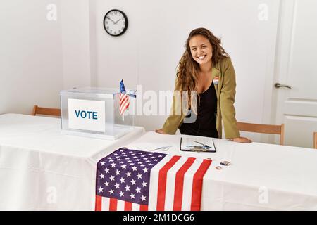 Junge, wunderschöne hispanische Frau, Wahlpräsidentin, die selbstbewusst am Wahlkollegium lächelt Stockfoto