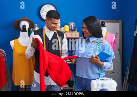 Mann und Frau Schneiderinnen halten Touchpad und T-Shirt im Nähstudio Stockfoto