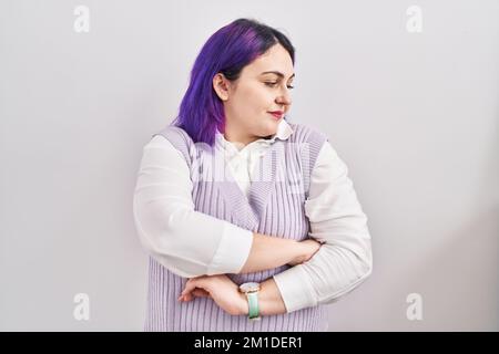 Große Frau mit lila Haaren, die auf weißem Hintergrund steht und zur Seite blickt, mit überkreuzten Armen überzeugt und selbstbewusst Stockfoto