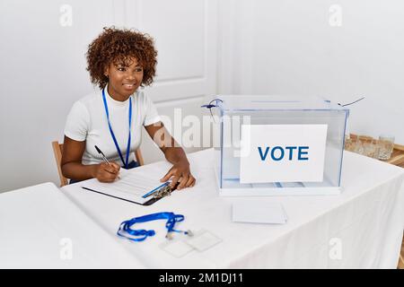 Junge afroamerikanische Frau, die am Wahlkollegium lächelnd selbstbewusst auf die Checkliste schreibt Stockfoto