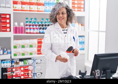 Grauhaarige Frau im mittleren Alter, Apothekerin, die in der Apotheke eine Tablettenflasche scannt Stockfoto
