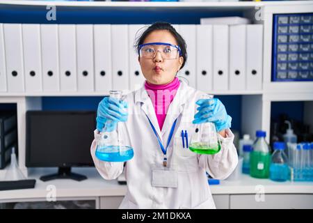 Junge asiatische Frau, die im Wissenschaftlerlabor arbeitet, macht Fische mit Mund und blinden Augen, verrückt und komisch. Stockfoto