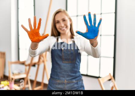 Junge kaukasische Frau lächelt selbstbewusst und zeigt bemalte Handflächen im Kunststudio Stockfoto