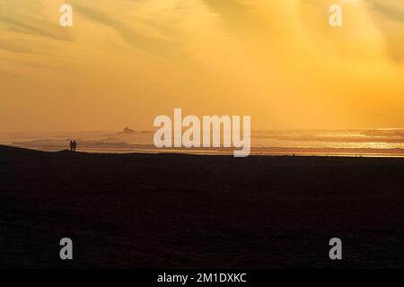 Ein Paar am Strand mit Blick auf die Ruinen des Wachturms Bordj El Berod am Horizont, Silhouetten bei Sonnenuntergang, symbolische Bilder Burgen aus Sand, Stockfoto