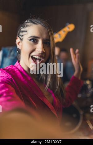 Eine begeisterte, stilvolle Sängerin macht während des Bandtrainings ein Foto von sich selbst. Musiker und Tonstudio-Konzept. Hochwertiges Foto Stockfoto