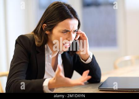 Wütende Geschäftsfrau, die telefonisch im Büro klagt Stockfoto