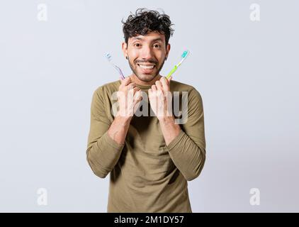 Ein gutaussehender Mann, der zwei Zahnbürsten isoliert hält. Ein lächelnder Typ, der zwei Zahnbürsten isoliert hält. Lächelnde Menschen, die zwei Zahnbürsten isoliert zeigen Stockfoto
