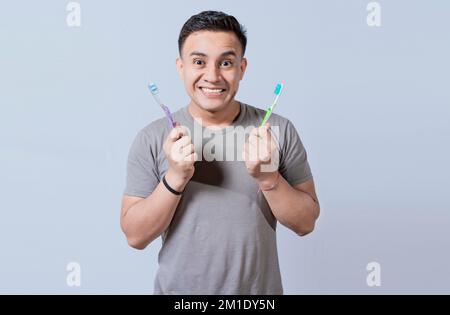 Ein lächelnder Typ, der zwei Zahnbürsten isoliert hält. Lächelnde Menschen, die zwei isolierte Zahnbürsten zeigen, attraktiver Mann, der zwei isolierte Zahnbürsten hält Stockfoto