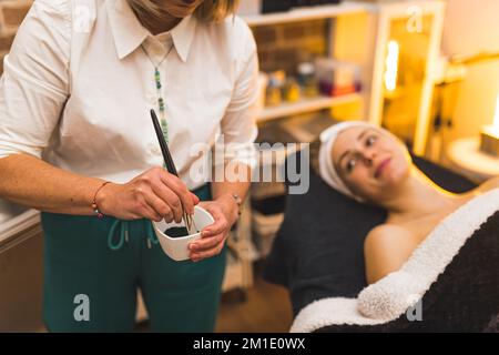 Kosmetikerin, die Gesichtsmaske auf dem Gesicht einer Frau aufträgt. Hochwertiges Foto Stockfoto