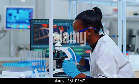 Afrikanische Frau Biochemikerin mit Mikroskop im modern ausgestatteten Labor. Schwarzer Wissenschaftler, Arzt, der mit verschiedenen Bakterien, Gewebe, Blutproben, pharmazeutischer Forschung für Antibiotika arbeitet Stockfoto