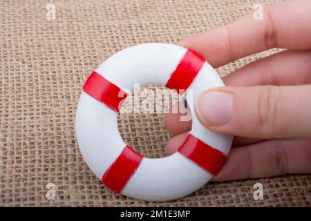 Hand, die einen Lifesaver oder eine Rettungsweste auf einem Stoffhintergrund hält Stockfoto