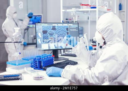 Mikrobiologe gekleidet in ppe, untersucht Blutprobe während des Coronavirus-Tests. Arzt, der mit verschiedenen Bakterien und Geweben arbeitet, pharmazeutische Antibiotikaforschung gegen covid19. Stockfoto