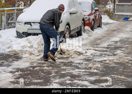 An einem Wintertag reinigt ein Mann mittleren Alters das Gebiet mit einer Schaufel von Schnee und Eis. Speicherplatz kopieren. Stockfoto