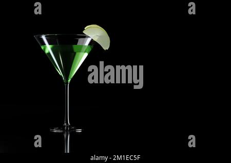 Grüner Appletini-Cocktail mit Apfelgarnierung in martini-Glas auf schwarzem Hintergrund Stockfoto