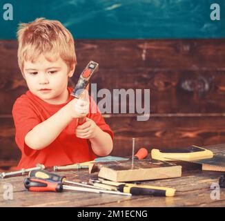 Das Kind ist niedlich und niedlich, wenn es als Baumeister oder Reparateur, als Reparateur oder als Handwerker spielt. Handwerkskunst. Ein Junge hämmert einen Nagel in das Holzbrett Stockfoto