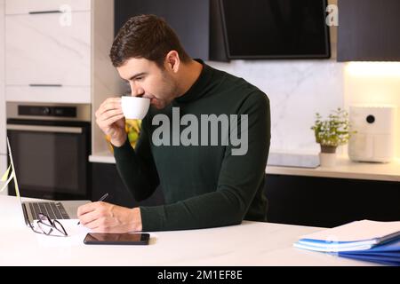 Ein Mann, der eine Tasse Kaffee trinkt, während er von zu Hause aus arbeitet Stockfoto