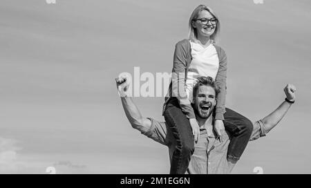 Seelenverwandte genießen gemeinsam die Freiheit. Verliebte Paare genießen die Freiheit an einem sonnigen Tag im Freien. Der Mann trägt eine Freundin auf den Schultern, Himmelshintergrund. Ein glückliches Paar Stockfoto