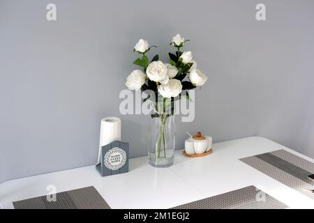 Moderne, stilvolle Einrichtung des Esszimmers in sanften Pastelltönen mit weißen Möbeln und Rosenstrauß in Vase auf dem Tisch Stockfoto