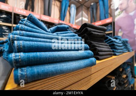 Nahaufnahme von vielen Jeans in den Regalen im Laden. Ein Haufen Jeans auf dem Regal. Konzept des Einkaufs, Verkaufs, Einkaufs und Jeans. Stockfoto
