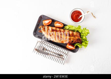 Draufsicht auf die köstlichen, saftigen Rippchen des Grills auf einem Keramiktablett mit frischem Gemüse. Gegrillte Schweinerippchen. Soße in einer Schüssel. Platz für Text Stockfoto