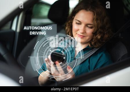 Weibliche Fahrerin steuert ein autonomes Auto mit einem Smartphone Stockfoto