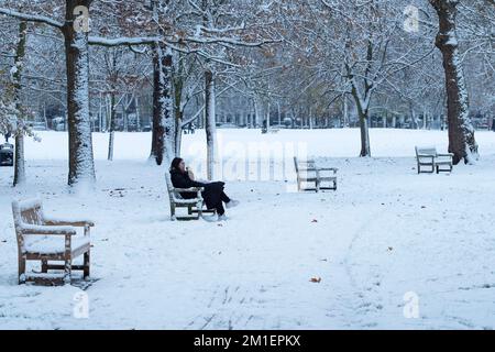 London , Vereinigtes Königreich . Eine Frau sitzt auf einer Bank in einem schneebedeckten Queens Park. West-London-Pendler durch London stehen vor der Herausforderung, am Dezemb zur Arbeit zu kommen Stockfoto