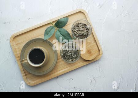 Getrocknete Teeblätter in einem Behälter und Teetasse auf dem Tisch Stockfoto