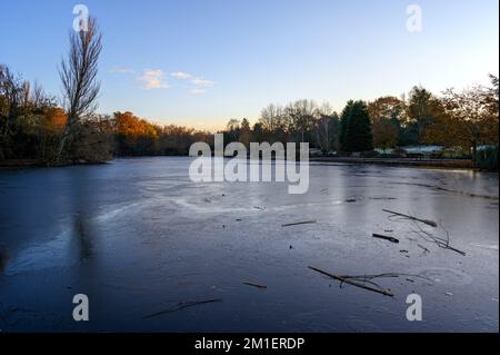 Ein gefrorener See bei Sonnenuntergang. In dieser Winterszene befindet sich Eis auf der Oberfläche des Sees. Ein kalter Wintertag in Kelsey Park, Beckenham, Kent, Großbritannien. Stockfoto